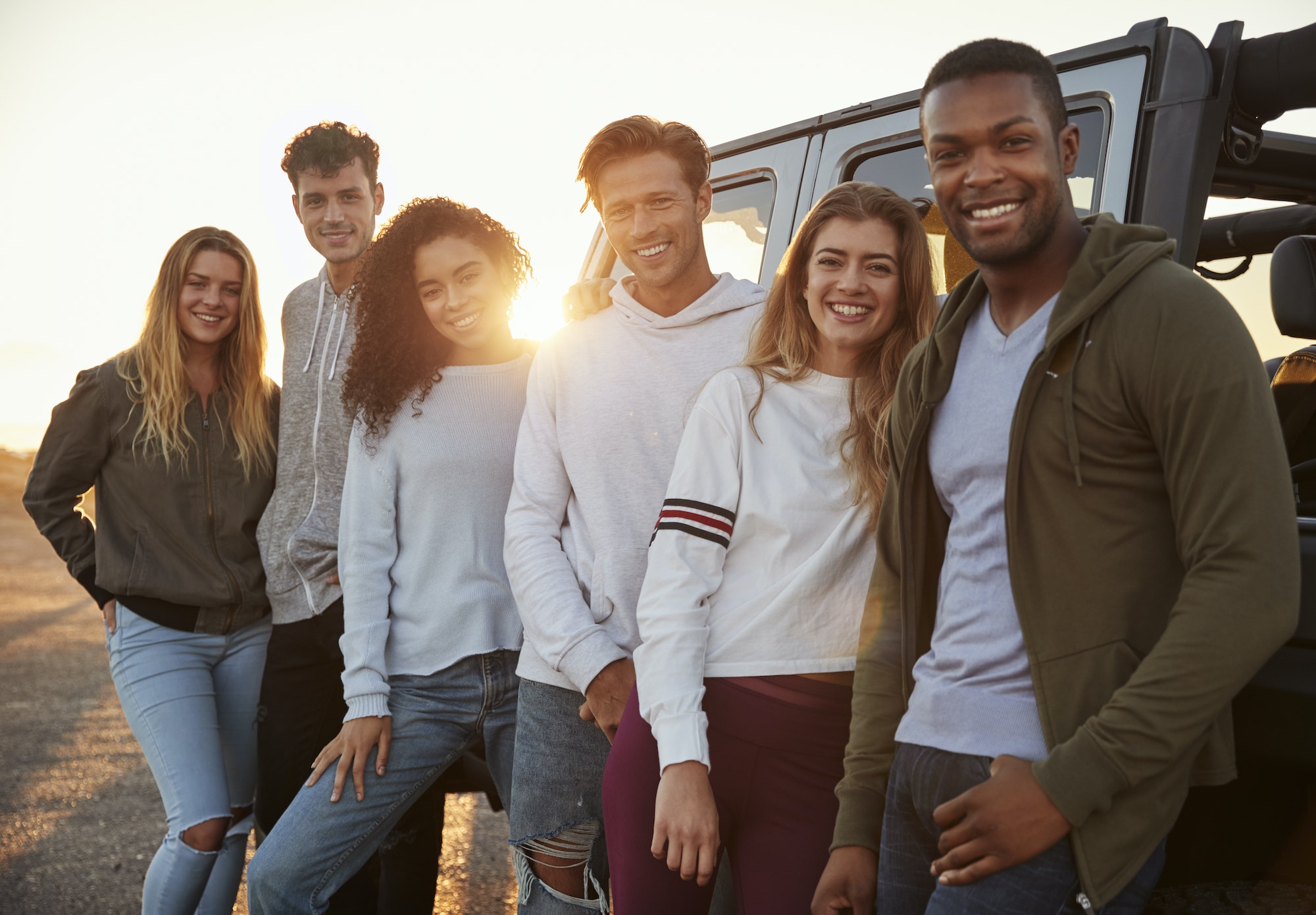 Young adult friends on a road trip standing by jeep, close up